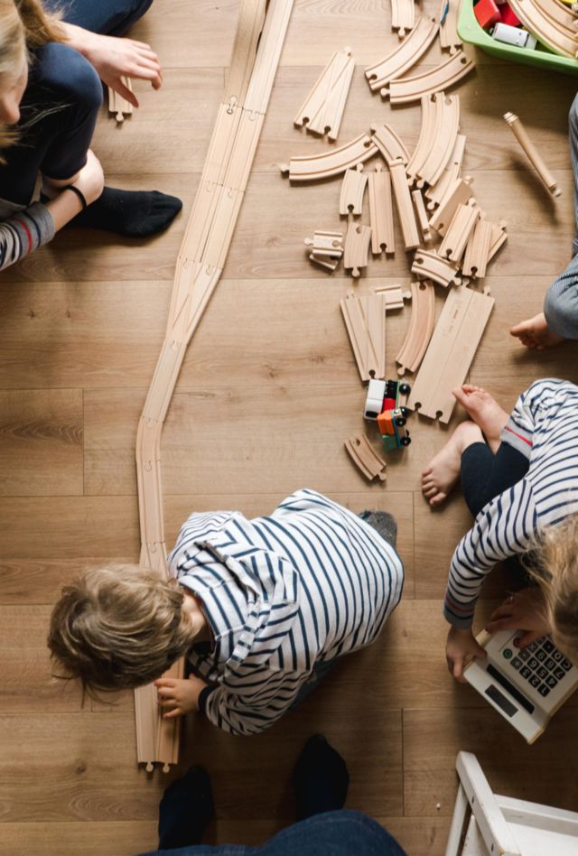 group of kids playing with wooden train tracks as caregivers look on