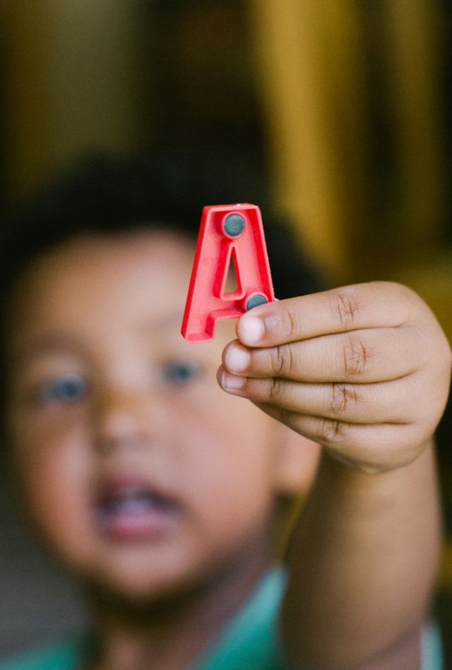 A child holds up a magnetic red plastic letter A
