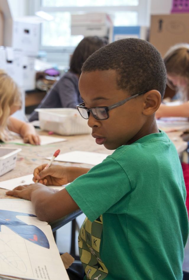 A group of children sit at a table with picture books and writing materials