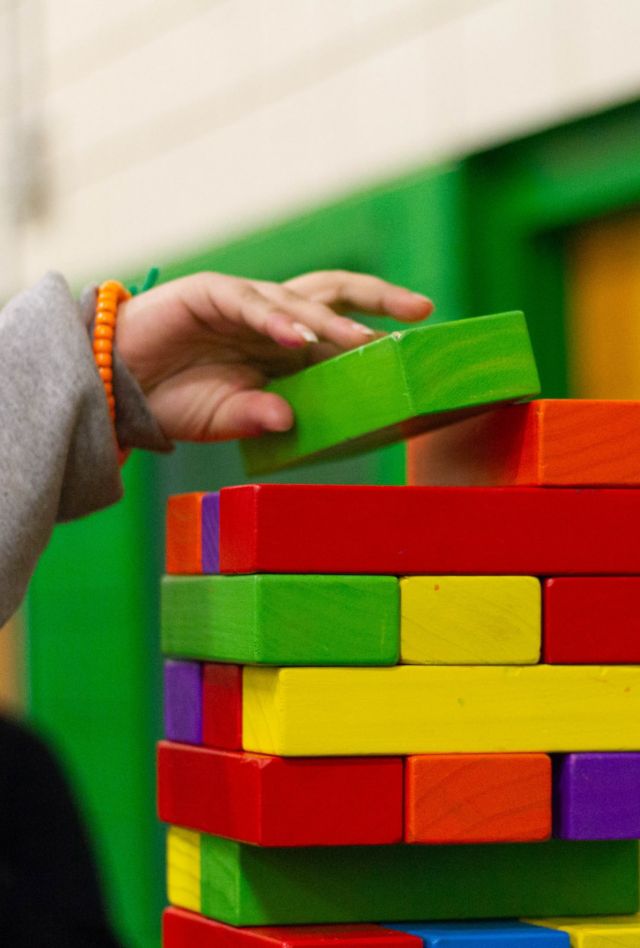 A hand places a block on top of a tower of brightly colored wooden blocks