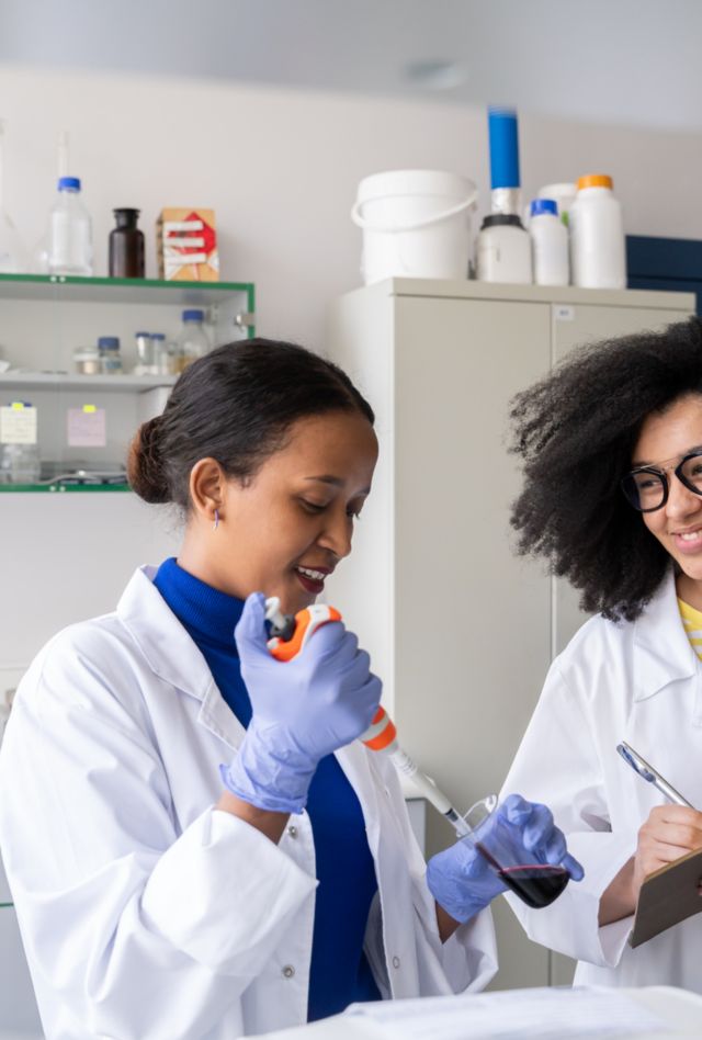 Two researcher wearing lab coats working with sample in lab.