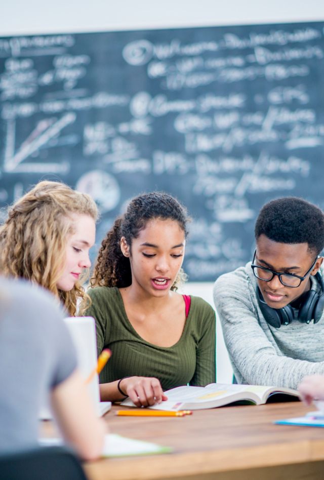 A young girl of african descent studies with her friends in class. They are all focused and working hard to complete their assignment.