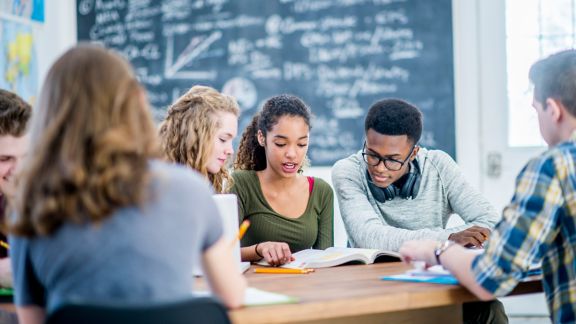 A young girl of african descent studies with her friends in class. They are all focused and working hard to complete their assignment.