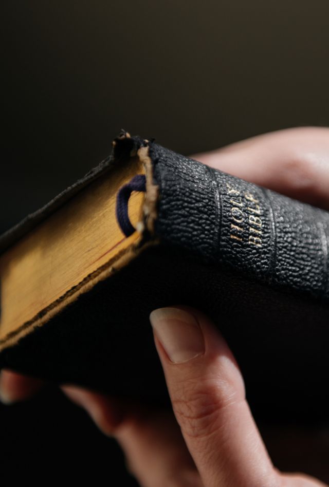 Woman holds an old, worn leatherbound Bible in her hands