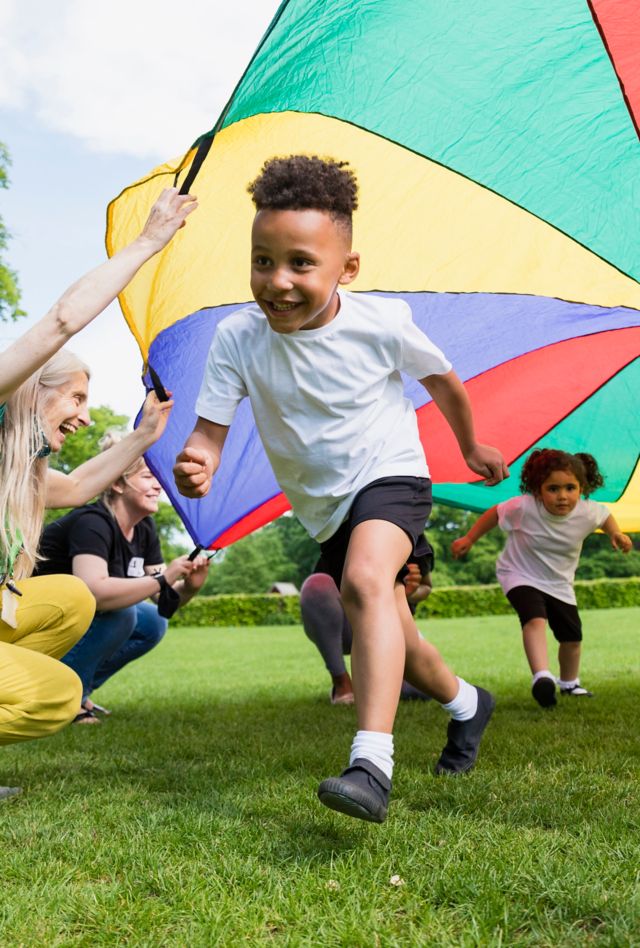 Children playing with a parachute at school during pe in the North East of England. A boy is running underneath it.