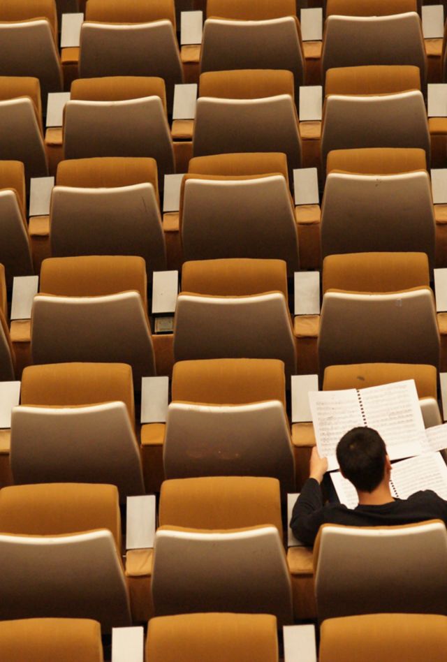 A student looks at papers while sitting in one of many chairs arranged in rows