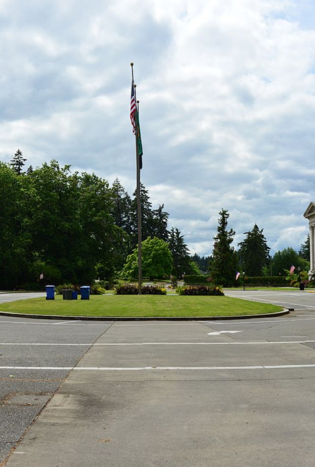 A traffic circle with a small grassy area with an American flagpole in the center. On the edges of the circle are stone buildings in the Federal style with large columns on the front facade