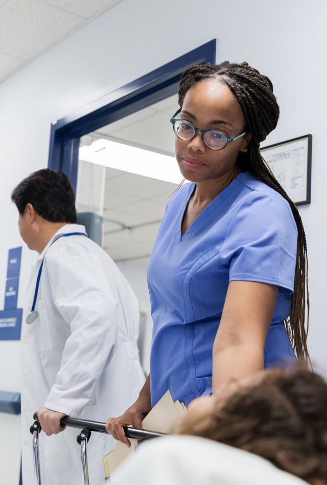 The mid adult female nurse turns to comfort the unrecognizable girl as she and the senior adult doctor wheel her down the hospital corridor.