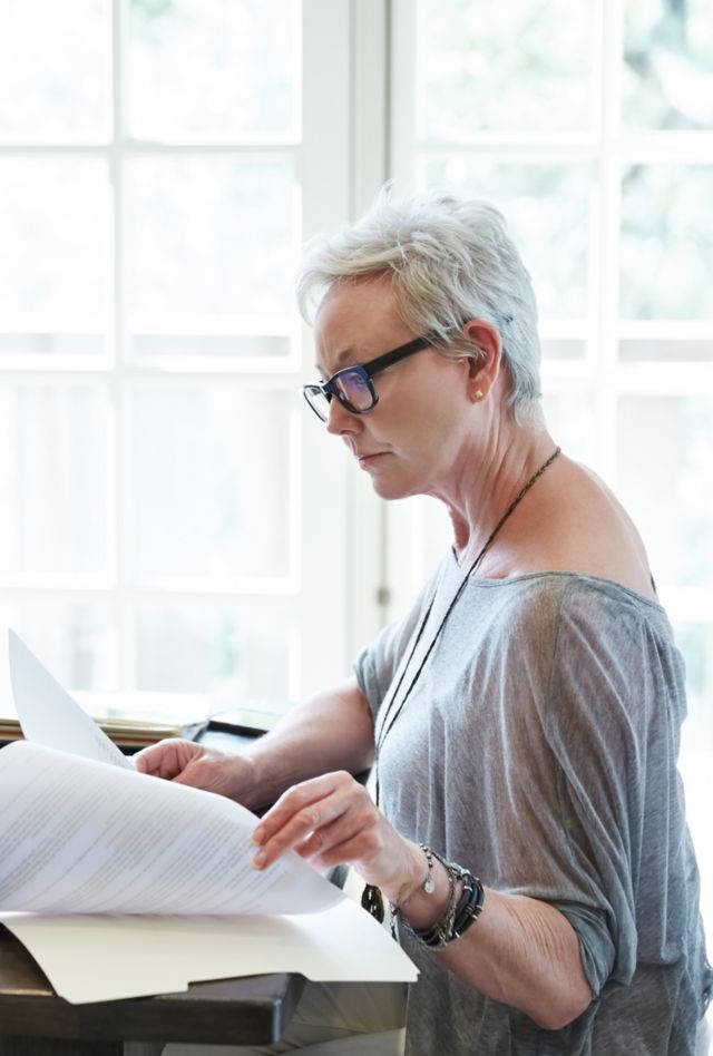 Older woman sitting at a table with a laptop and some papers