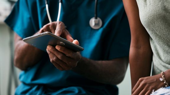 Close up of health care worker in scrubs looking at a tablet with a patient