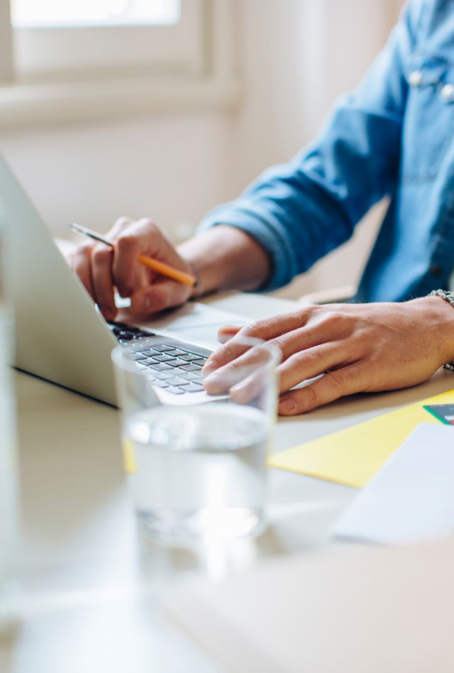 Anonymous man in casual clothes sitting at table and typing on laptop keyboard while working on remote project at home