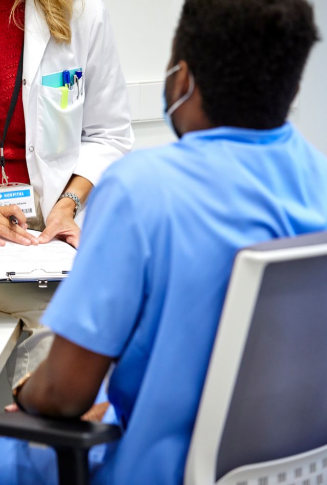 Anonymous nurse and a doctor wearing masks talking at the hospital reception desk