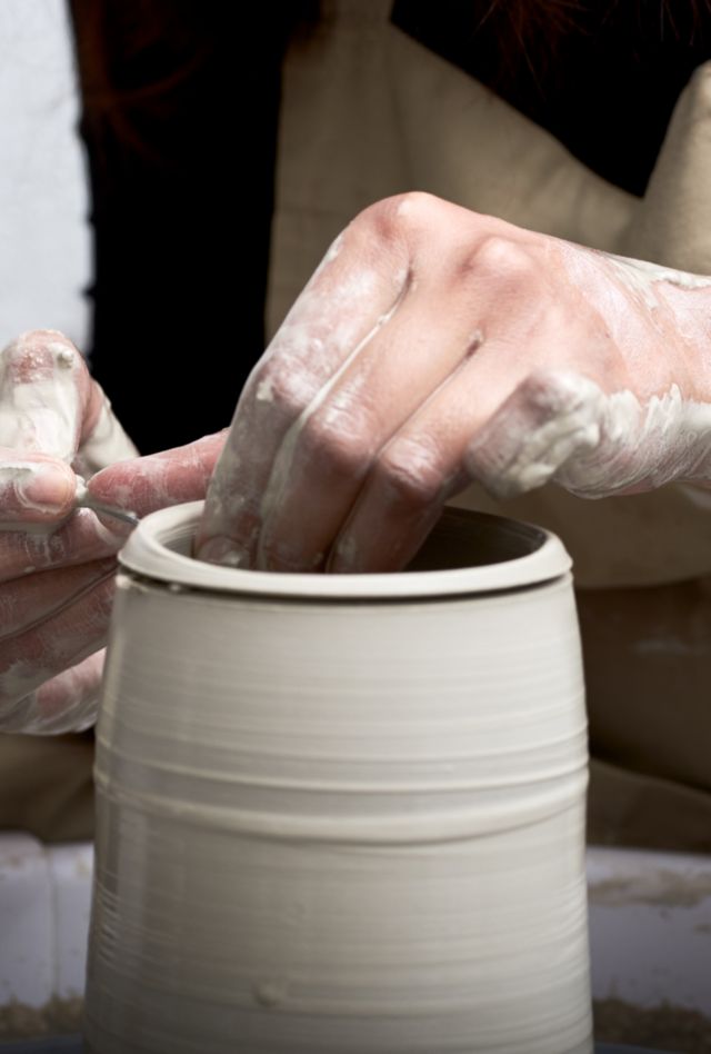Close-up of professional potter decorating clay vase on pottery wheel.
