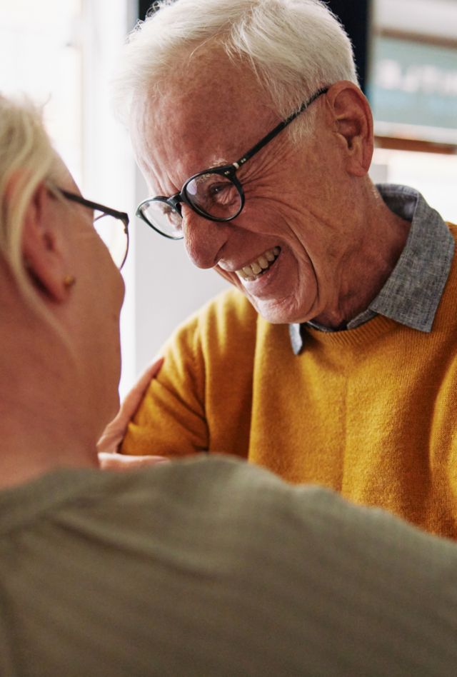 Closeup of a senior man laughing while greeting a female friend with a hug during a visit together