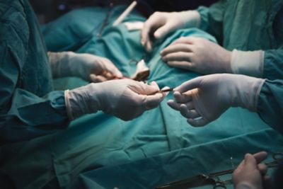 Unrecognisable Medical team performing surgery close up in the action - Hands with white gloves - green scrubs.