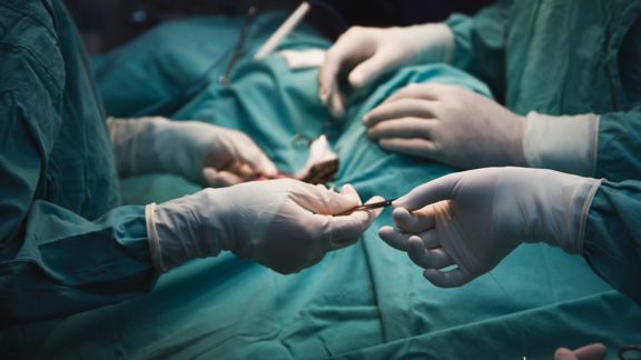 Unrecognisable Medical team performing surgery close up in the action - Hands with white gloves - green scrubs.