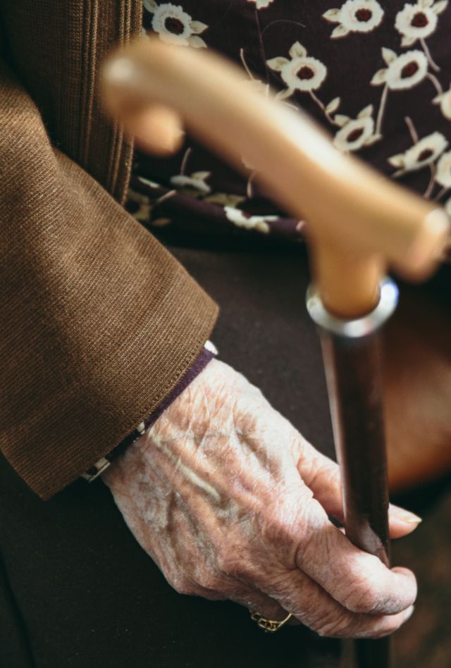 A person with wrinkled hands sits holding a cane