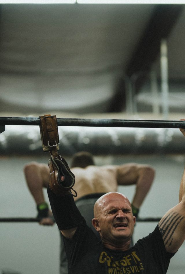 A person with a prosthetic arm does a pullup at a bar in a gym.