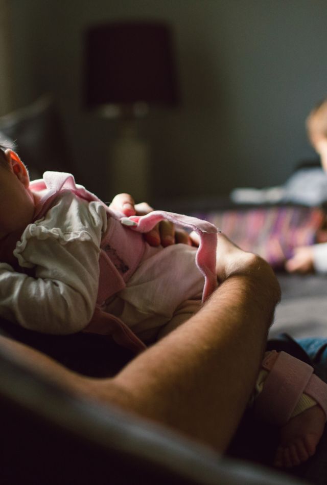 A person holds a baby while an older child play behind them