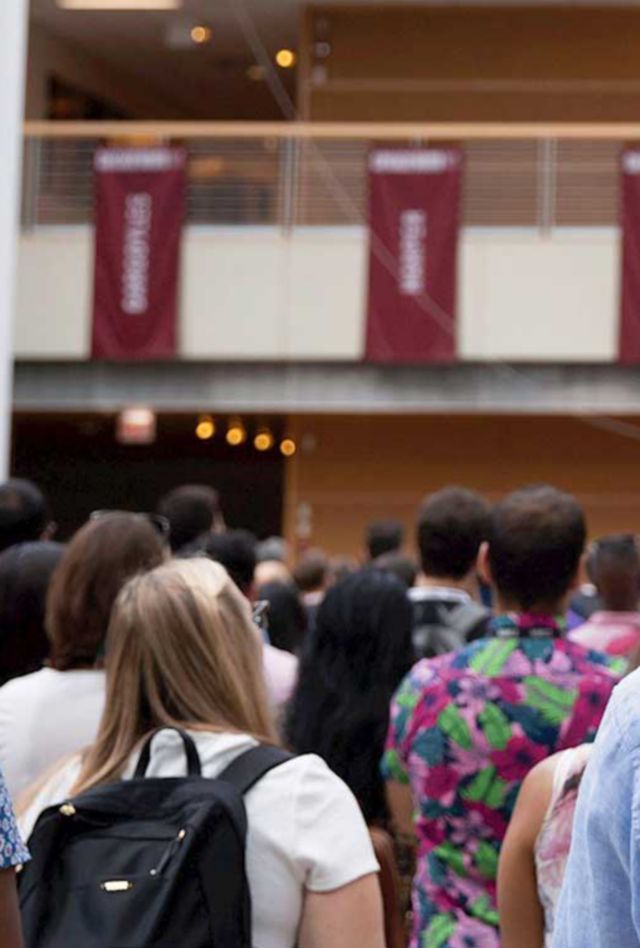 A crowd of people stands in front of a balcony bearing the Booth School of Business logo