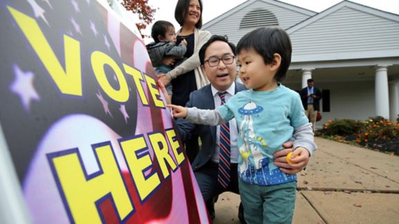 Asian family in front of a Vote Here sign