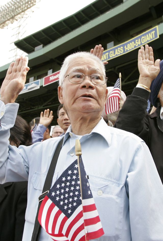 A group of AAPI individuals at an event, holding American flags and raising their hands