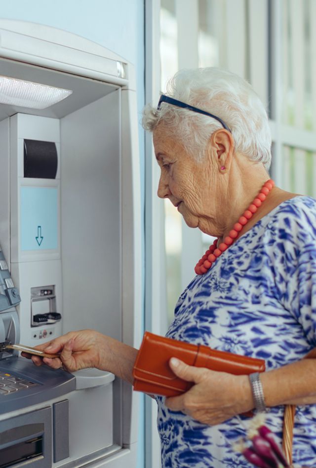 Image of woman with short white hair and classes putting card into an ATM