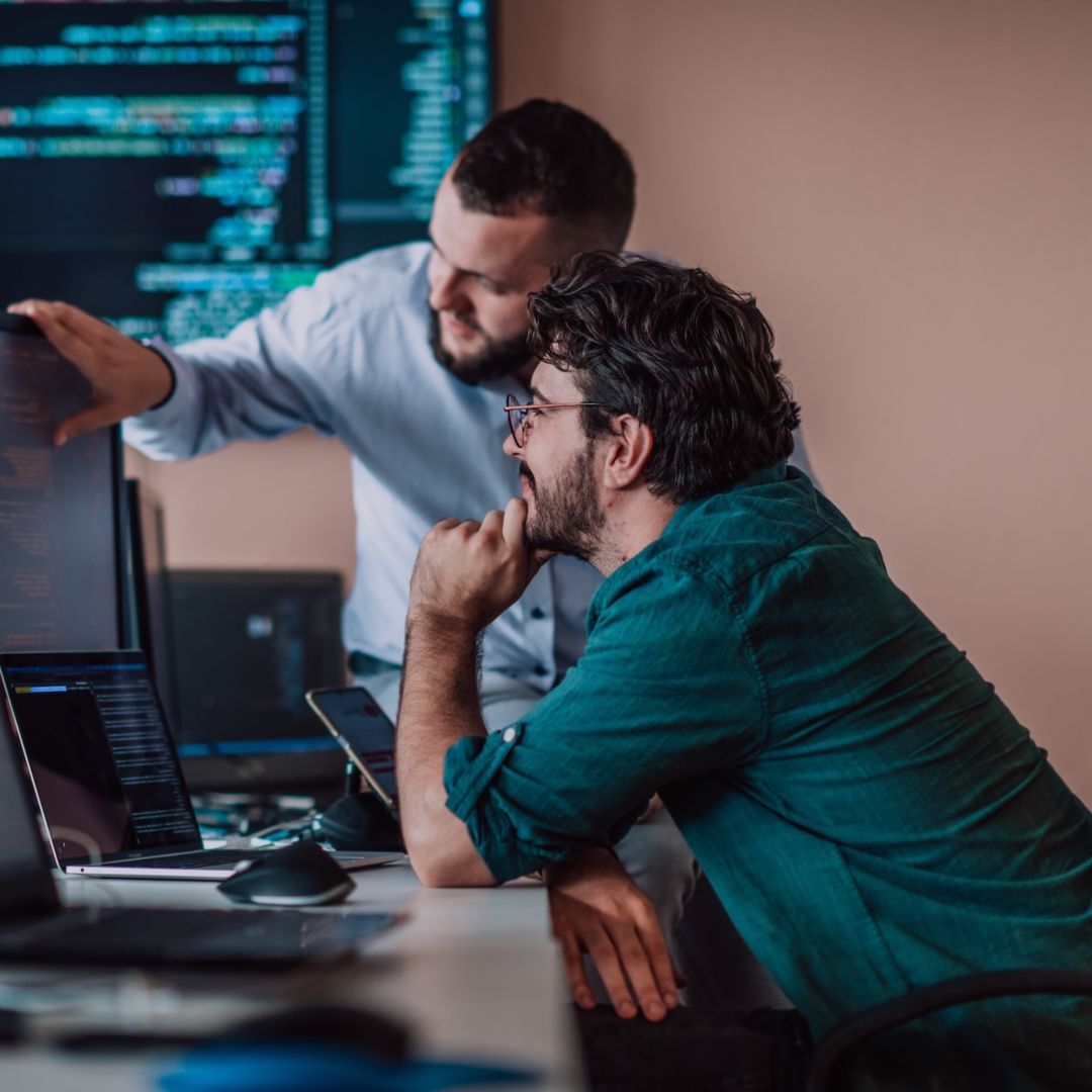 Two people looking at programming code on a computer screen in an office