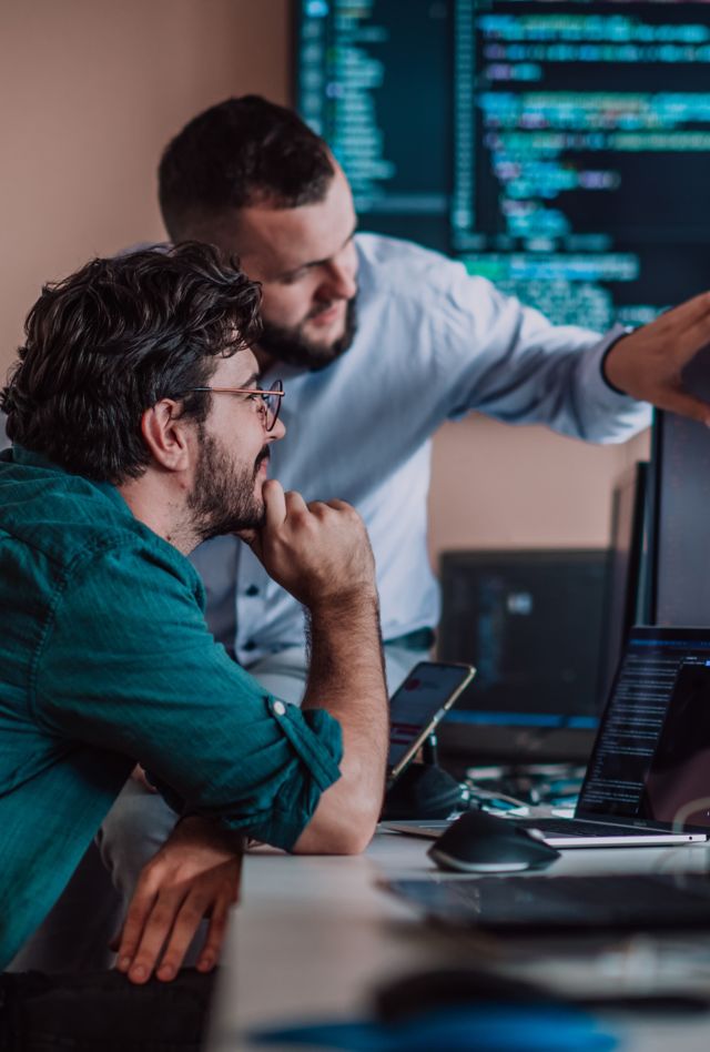 Two people looking at programming code on a computer screen in an office