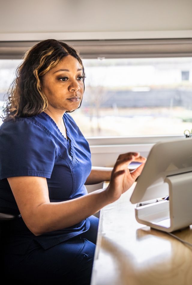 Woman wearing scrubs at a desk looking at a tablet