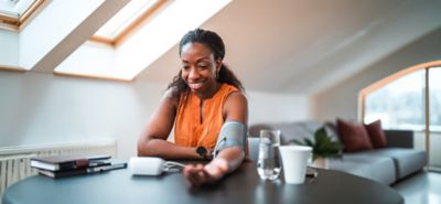 Mid adult black female using a medical device in a domestic dining room. Measuring blood pressure at home.