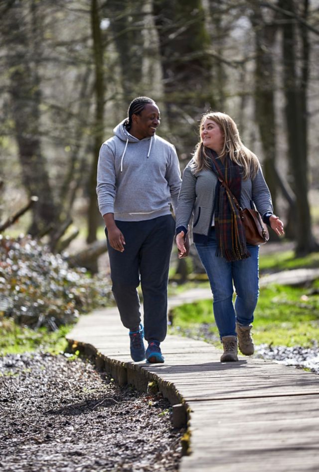 Man and woman walking on a wooded path, smiling