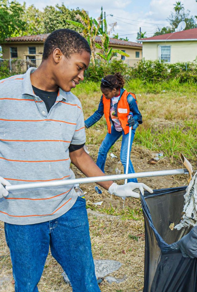 2GJJR18 Miami Florida,Little Haiti,volunteers working together teamwork neighborhood clean up,student teen teenager Black boy male female collecting litter