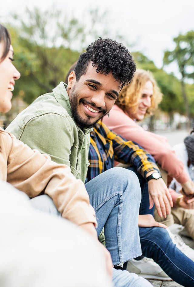 Diverse group of young people laughing together - Hispanic latin man smiling at camera while having fun with multiracial friends in city street - Friendship, unity and millennial colleagues concept