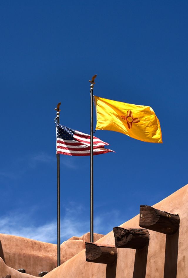 An American flag and a New Mexico state flag fly an adobe-style building