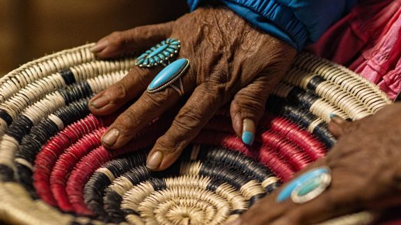 An Elderly Native American Woman (Navajo) Wearing Turquoise Rings on Her Fingers Touches a Woven Navajo Basket