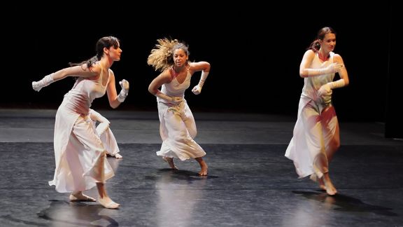 Three women in white dresses dancing on a black stage