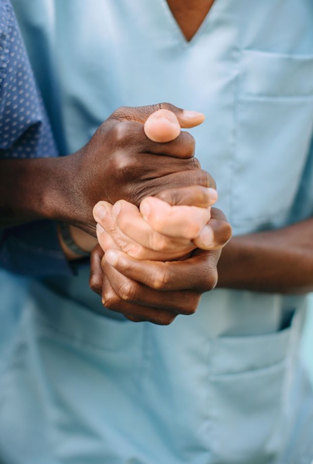 Close up of a health care provider in scrubs grasping hands with a patient