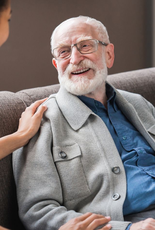 female caregiver talking chatting to smiling senior man on a couch