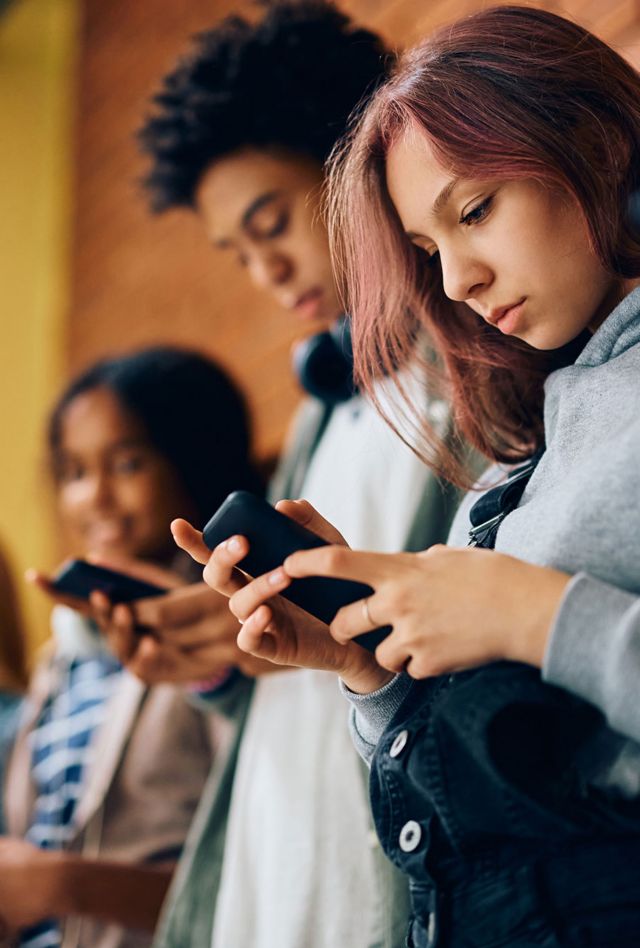 High school student and her friends using their smart phones in a hallway.