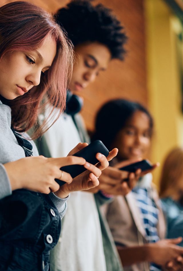 High school student and her friends using their smart phones in a hallway.