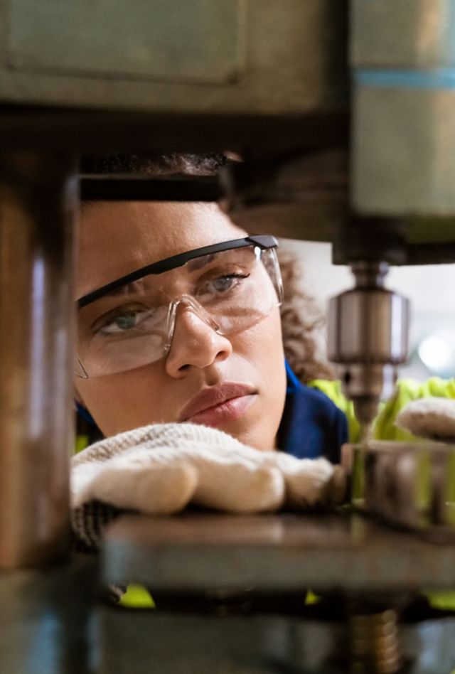 Close-up of female apprentice using yoke machine. Female engineer is wearing protective glasses in factory. She is working in manufacturing industry.