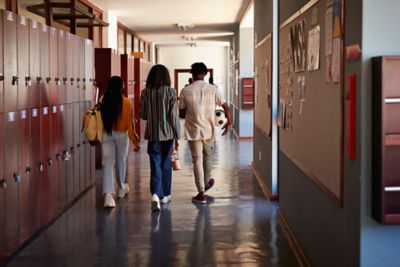 Full length rear view of male and female students walking together in corridor with lockers at high school