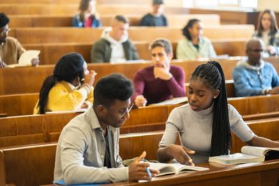 A class of scholars sitting at  their desks in a traditional amphitheater classroom, working together during study time