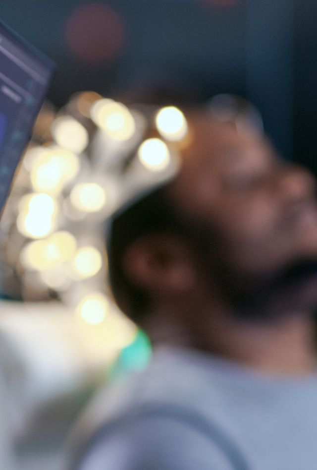 Monitors Show EEG Reading and Graphical Brain Model. In the Background Man Wearing Brainwave Scanning Headset Sits in a Chair with Closed Eyes