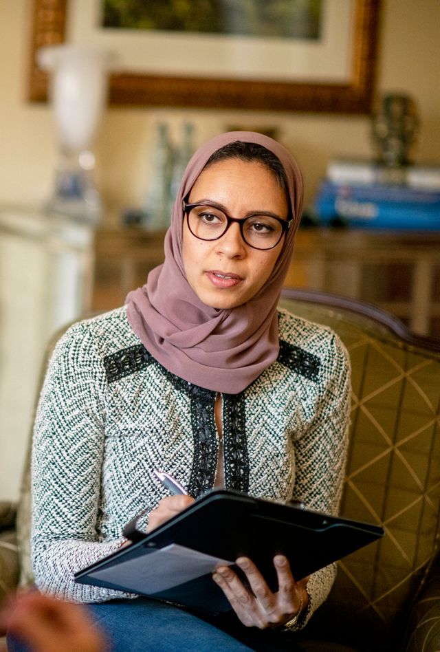 Young woman wearing a hijab taking notes as she listens to another person