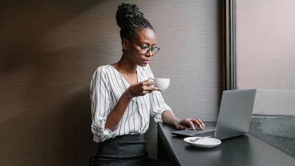 Woman holding a mug while looking at a laptop
