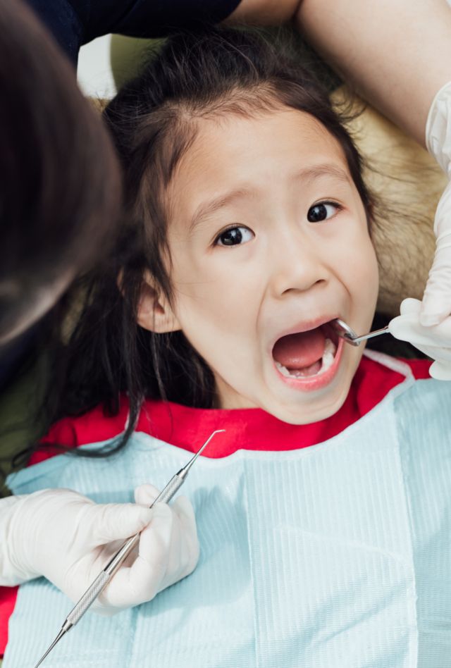 Young female dentist examining kids teeth in dentist's office