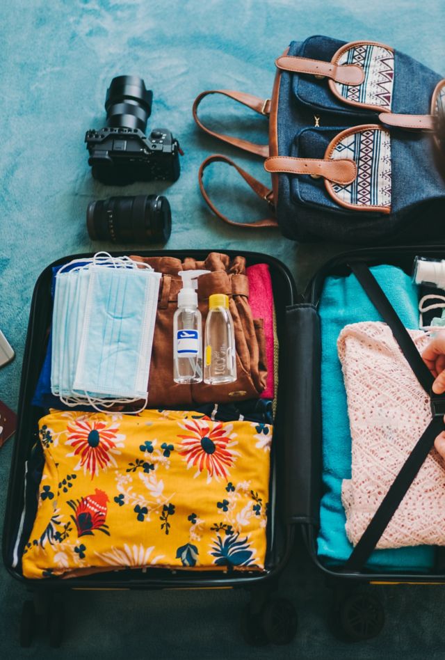 Woman packing suitcase for summer travel, including face masks and airplane travel-sized antibacterial hand gels