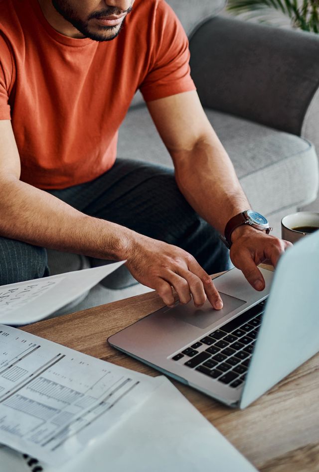 Man and woman sitting on the couch reviewing bills and working on a laptop